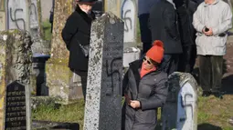 Seorang wanita melihat kondisi salah satu nisan yang dicoreti lambang swastika Nazi di pemakaman Yahudi, Westhoffen, dekat Strasbourg, Prancis, Rabu (4/12). Sedikitnya 107 makam menjadi sasaran vandalisme dengan dicoreti lambang swastika Nazi. (AFP/Patrick Hertzog)