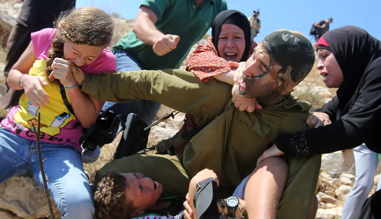 Foto yang diambil pada 28 Agustus 2015 menunjukkan Ahed Tamimi (kiri) menggigit tangan tentara Israel saat berkelahi bersama keluarganya karena terjadi bentrokan di Desa Nabi Saleh. (AFP Photo/Abbas Momani)