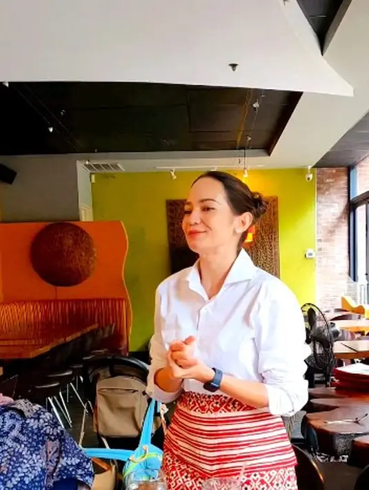 Enzy tampak cantik dalam balutan kemeja putih dengan bawahan kain etnik warna merah.