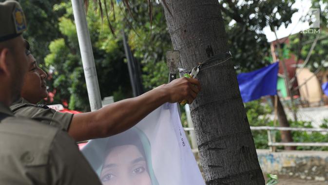 Petugas Satpol PP mencabut paku yang digunakan untuk memasang APK yang terpasang di Jalan Raya Bogor dekat GOR Ciracas, Jakarta, Rabu (23/1). Penurunan APK ini karena pemasangannya dianggap melanggar ketentuan. (Liputan6.com/Helmi Fithriansyah)