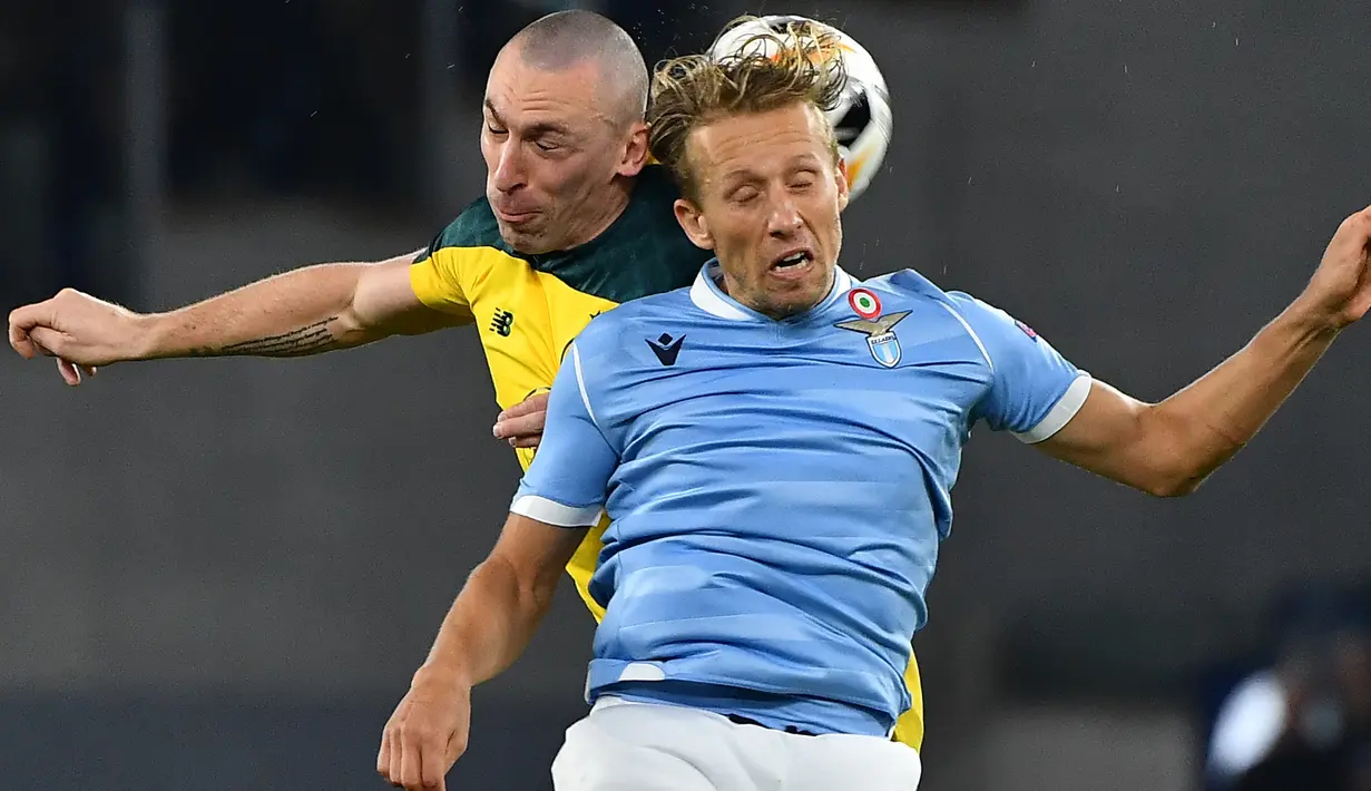 Gelandang Celtic, Scott Brown menyundul bola saat berebut dengan pemain Lazio Lucas Leiva pada matchday keempat Grup E Liga Europa 2019 di Stadion Olympico, Kamis (7/11/2019). Celtic mengalahkan Lazio 2-1 untuk kemudian melaju ke babak 32 besar. (Tiziana FABI / AFP)