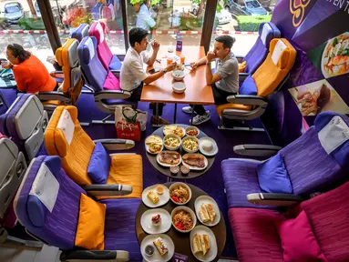 Orang-orang duduk di kursi pesawat saat makan di restoran pop-up bertema kabin pesawat di kantor pusat Thai Airways di Bangkok, 10 September 2020. Restoran pop-up ini menyajikan sekitar 2.000 makanan per hari untuk memulihkan pendapatan yang hilang selama pandemi virus corona. (Mladen ANTONOV/AFP)