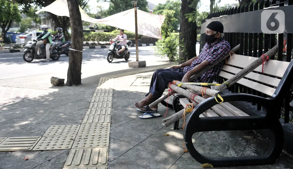 Warga nekat duduk di bangku trotoar yang disegel garis pembatas dan ditutupi bambu di kawasan Rawamangun, Jakarta, Minggu (3/5/2020). Bangku trotoar di sepanjang jalan Rawamangun disegel untuk mencegah kerumunan warga sebagai upaya memutus rantai penyebaran COVID-19. (merdeka.com/Iqbal S. Nugroho)