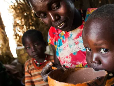 Seorang wanita bernama Nybol Madut memberi minum semangkuk alkohol lokal kepada anaknya di tempat penampungan di Sudan Selatan (22/11). (AFP Photo/Albert Gonzalez Farran)