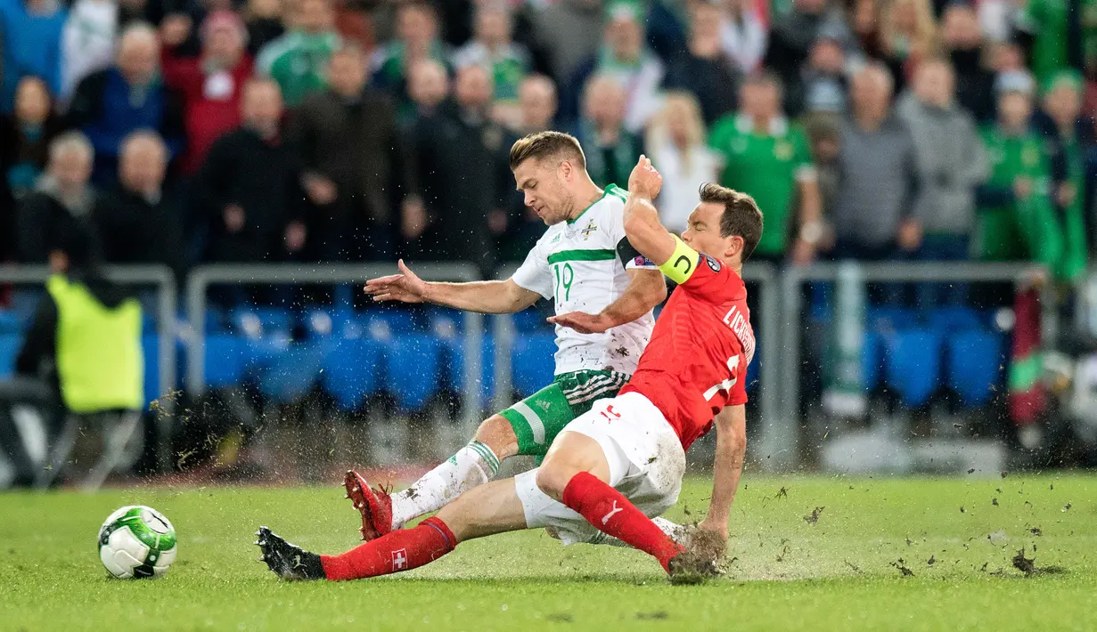 Gelandang Irlandia Utara, Jamie Ward dan pemain Swiss, Stephan Lichtsteiner berebut bola pada playoff Piala Dunia 2018 zona Eropa di St Jakob Park Stadium, Minggu (12/11). Swiss akhirnya lolos ke Piala Dunia 2018. (Laurent Gillieron/Keystone via AP)