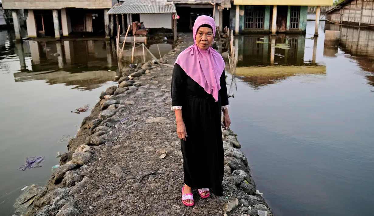 Kumaison berdiri di jalan setapak menuju rumahnya di lingkungan banjir di Timbulsloko, Jawa Tengah, Indonesia, 30 Juli 2022. Kumaison mengatakan rumahnya telah ditinggikan dengan beton dan tanah sampai tiga kali karena banjir yang lebih tinggi. (AP Photo/Dita Alangkara)