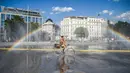 Seorang pesepeda melewati semprotan air di Schwarzenbergplatz di Wina, Austria (28/7/2020). Suhu tertinggi di Wina mencapai angka 37,2 derajat Celsius pada Selasa (28/7). (Xinhua/Guo Chen)