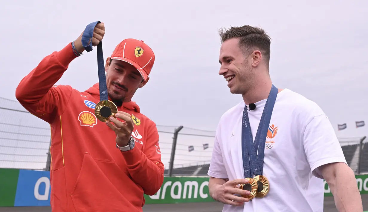 Pembalap Ferrari, Charles Leclerc berbincang sambil memegang medali emas Olimpiade Paris 2024 milik atlet balap sepeda track Belanda, Harrie Lavreysen menjelang Formula 1 GP Belanda di Sirkuit Zandvoort, Kamis (22/08/2024) waktu setempat. (AFP/John Thys)