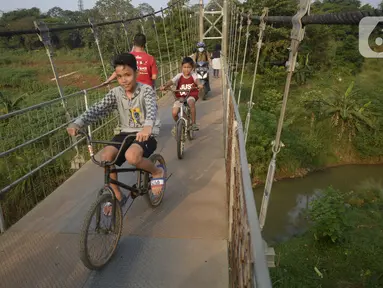 Anak-anak bersepeda melintasi jembatan gantung di Kelurahan Curug, Bojongsari, Kota Depok, Jawa Barat, Senin (24/8/2020). Setiap sore, warga sekitar bermain di jembatan tersebut sambil menikmati matahari tenggelam. (merdeka.com/Dwi Narwoko)