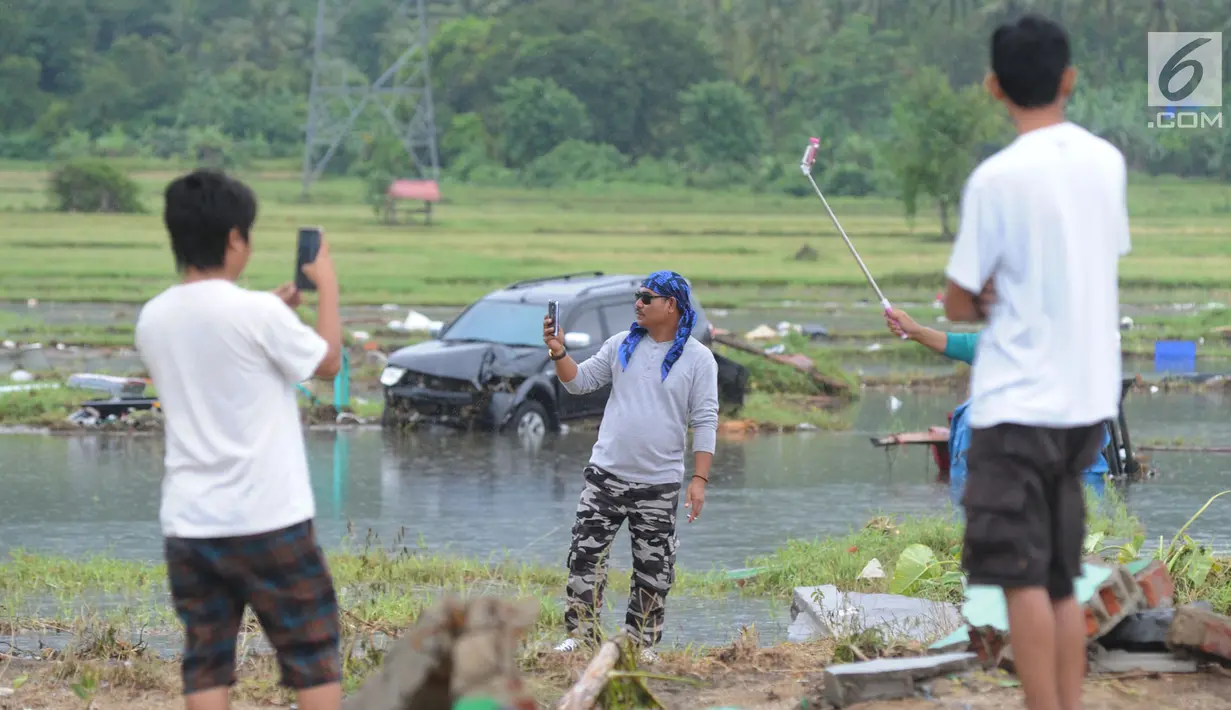 Warga berselfie dengan latar belakang kawasan terdampak bencana tsunami di Carita, Banten, Selasa (25/12). Libur Natal dimanfaatkan warga luar Anyer dan carita untuk menyaksikan langsung terdampak bencana sambil berselfie. (Merdeka.com/Arie Basuki)