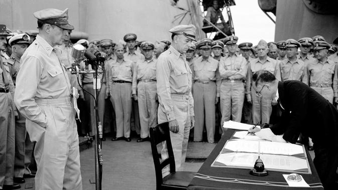 Jenderal AS Douglas MacArthur (kiri) menyaksikan Menteri Luar Negeri Jepang Manoru Shigemitsu menandatangani dokumen penyerahan di atas kapal perang USS Missouri, Teluk Tokyo, 2 September 1945. Penandatanganan ini menandai berakhirnya Perang Dunia II. (AP Photo/C.P. Gorry, File)