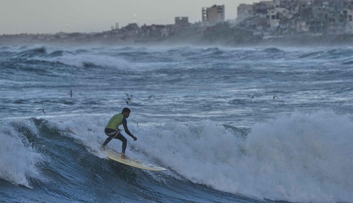 Meski, sepanjang garis pantai menunjukkan kerusakan nyata dengan puing-puing bangunan di sekitarnya. Tampak dalam foto, Khalil Abu Jayyab, warga Palestina, berselancar di pantai Kota Gaza, Minggu, 28 Desember 2025. (AP Photo/Jehad Alshrafi)