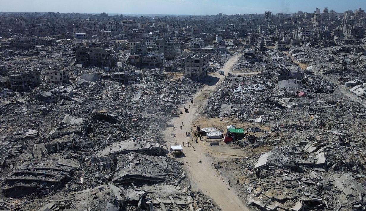 Foto udara yang diambil menggunakan pesawat tanpa awak atau drone memperlihatkan beberapa warga Palestina berjalan di sepanjang jalan yang dikelilingi oleh bangunan-bangunan yang hancur akibat serangan militer Israel selama dua tahun terakhir di Kota Gaza, Rabu 15 Oktober 2025. (AP Photo)