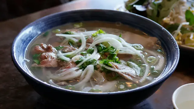 Semangkuk pho bo khas Vietnam dengan kuah kaldu sapi hangat, mi beras, irisan daging, dan taburan rempah segar.