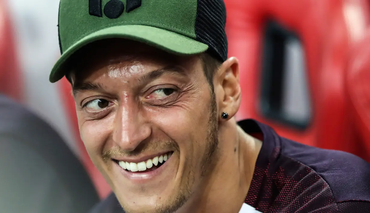 Gelandang Arsenal, Mesut Ozil tersenyum di bangku cadangan saat melihat rekannya bertanding melawan Atletico Madrid di International Champions Cup di Singapura (26/7). Arsenal kalah 3-1 setelah bermain 1-1 di waktu normal. (AP Photo/Yong Teck Lim)
