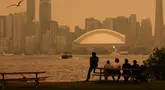 Warga memandang cakrawala pusat kota Toronto dari Kepulauan Toronto saat kabut asap akibat kebakaran hutan di Ontario Utara menyelimuti kota dan menurunkan kualitas udara, Toronto, Ontario, Kanada, Kamis, 15 Juli 2026. (AFP/ Cole Burston)