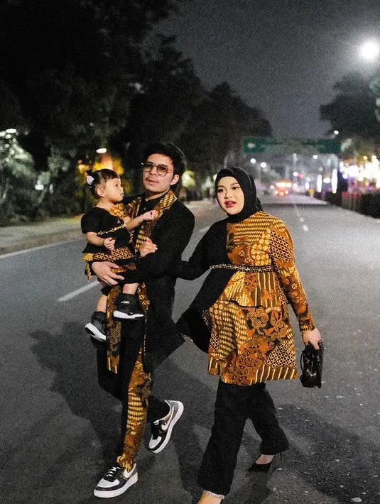 Aurel Hermansyah dan Atta Halilintar bersama Ameena serasi mengenakan batik. Aurel dengan atasan batik di satu sisi dan sisi lainnya warna hitam serasi dengan celananya. Atta mengenakan jas hitam dengan bagian depan batik serasi dengan celananya. [@aurelie.hermansyah]