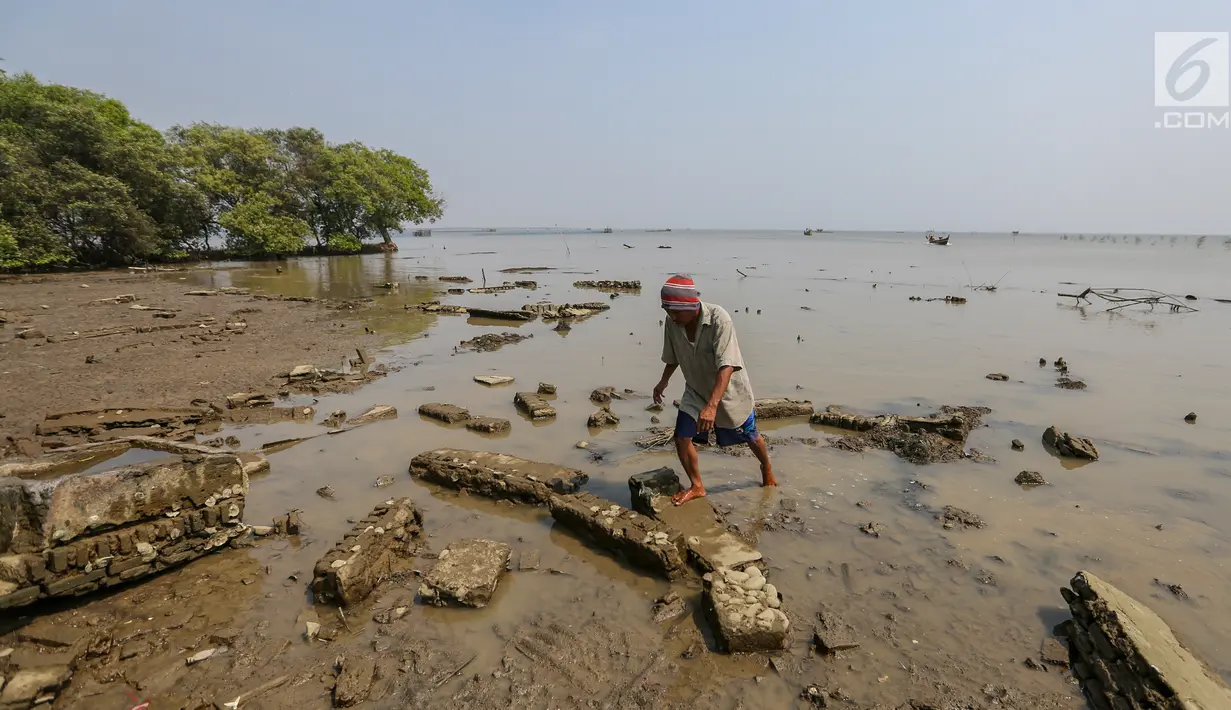 Warga melintas di atas puing bangunan yang terkikis akibat abrasi di Desa Pantai Mekar, Kecamatan Muara Gembong, Bekasi, Kamis (20/6/2019). Puluhan rumah warga di Kampung Muarajaya RT01/RW01 Desa Pantai Mekar hilang tersapu air saat terjadi abrasi selama 10 tahun. (Liputan6.com/Fery Pradolo)