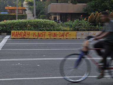 Pedagang siomay melintasi coretan "May Day Is Not Fun Day" di pembatas jalur bus Transjakarta kawasan Sarinah, Jakarta, Selasa (1/5). Aksi May Day di Jakarta meninggalkan jejak vandalisme yang dibuat kaum pekerja itu. (Merdeka.com/ Iqbal S. Nugroho)
