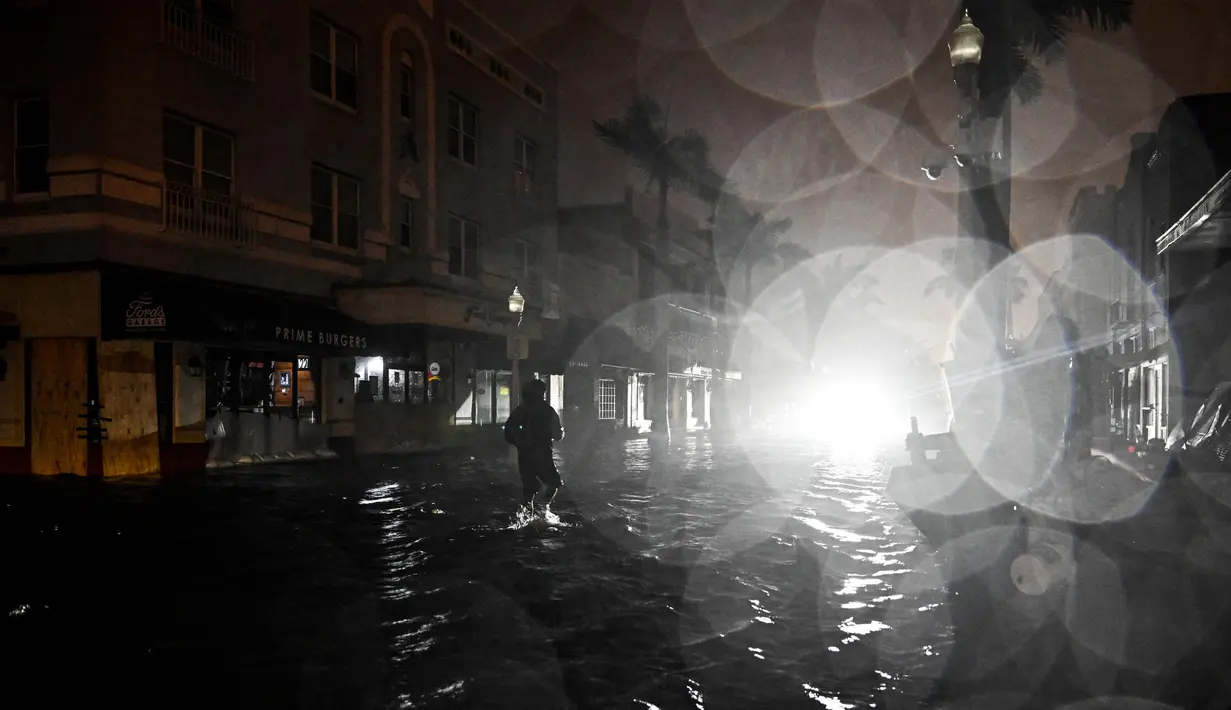 Seorang pria berjalan melewati jalanan yang tergenang air setelah Badai Milton mendarat di Fort Myers, Florida, pada tanggal 9 Oktober 2024. (CHANDAN KHANNA/AFP)