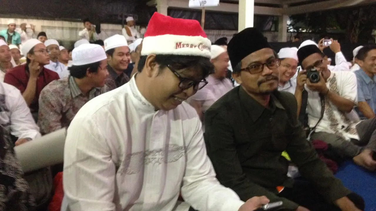 Pria bernama Alim memakai topi Santa Klaus berwarna merah putih lengkap dengan tulisan Merry Christmas saat Haul ke-7 Gus Dur. 