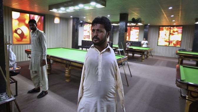 Mohammad Ikram, yang bermain snooker dengan dagunya, berjalan di klub snooker lokal di kota Samundri, Pakistan (25/10/2020). Ikram, 32, lahir tanpa lengan, tetapi semua orang mengagumi keterampilan snookernya ketika dia memukul bola dengan dagunya di atas meja snooker. (AP Photo/Anjum Naveed)