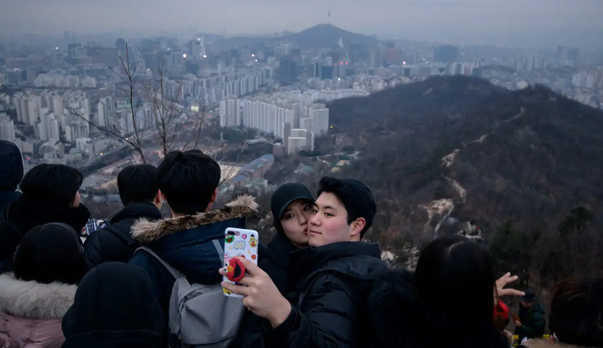 Pasangan berselfie di sudut pandang yang menghadap ke cakrawala kota untuk menyaksikan matahari terbit pertama tahun baru, meskipun dalam kondisi mendung, di Seoul, Korea Selatan (1/1/2020). (AFP/Ed Jones)