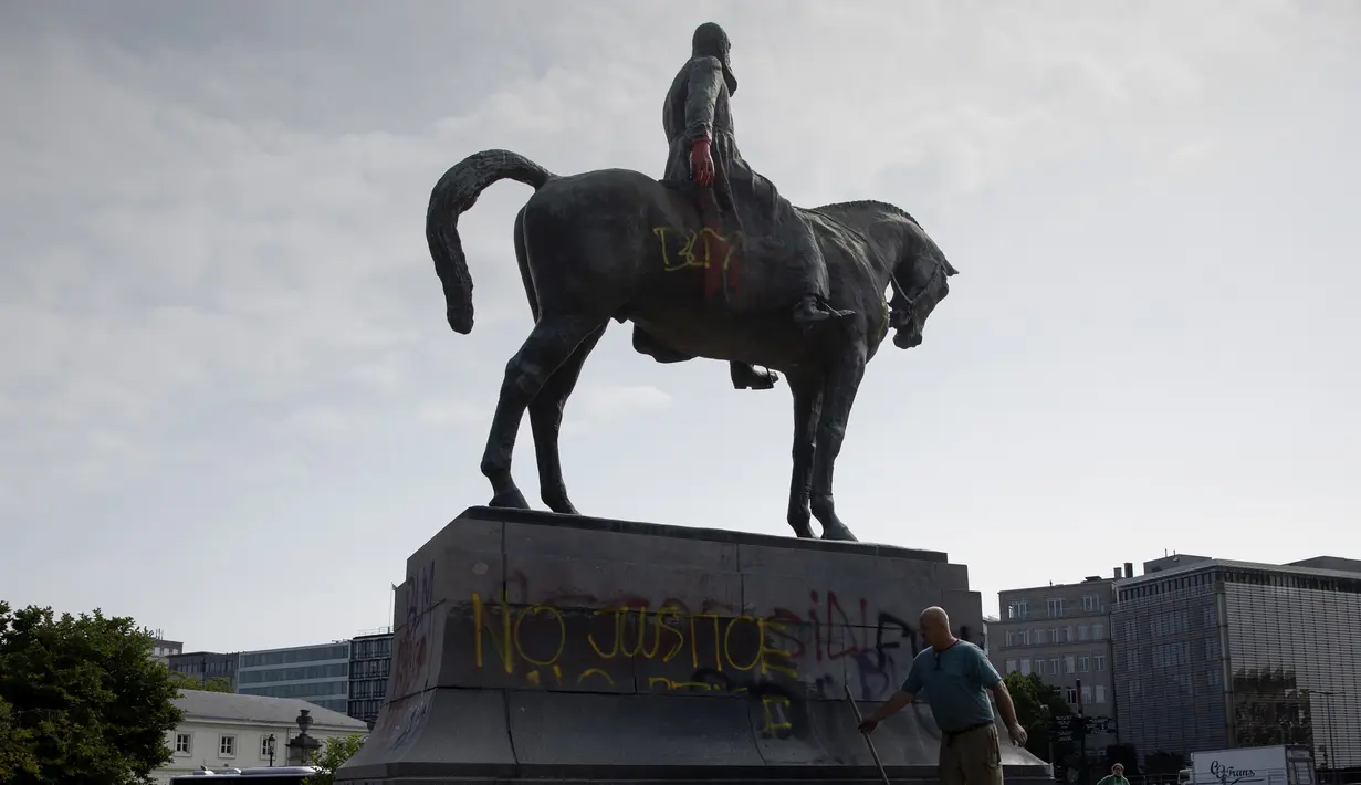 Seorang pria membersihkan coretan pada patung Raja Belgia Leopold II di Brussel, Belgia, Rabu (10/6/2020). Di tengah protes dunia atas kematian George Floyd, patung Raja Leopold II dirusak karena pemerintahannya yang brutal ketika menguasai Kongo ratusan tahun silam. (AP Photo/Virginia Mayo)