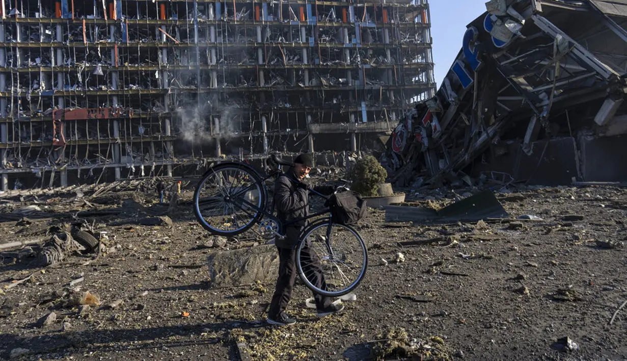 Seorang pria membawa sepedanya di tengah kerusakan setelah serangan sebuah pusat perbelanjaan di Kiev, Ukraina, Senin (21/3/2022). Delapan orang tewas dalam serangan tersebut. (AP Photo/Rodrigo Abd)