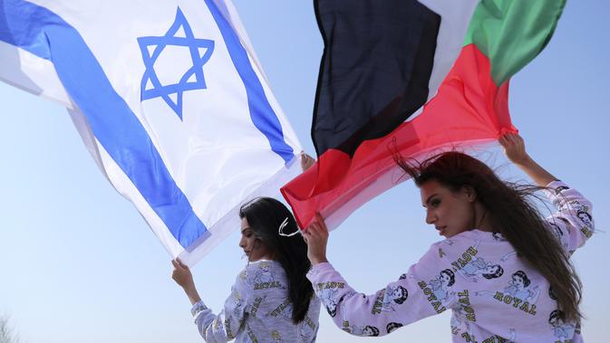 Model Israel May Tager (kiri) mengibarkan bendera Israel dan model Dubai asal Rusia Anastasia Bandarenka mengibarkan bendera Uni Emirat Arab saat pemotretan di Dubai, Uni Emirat Arab, 8 September 2020. Fix, merek pakaian dalam dan piyama Israel melakukan pemotretan di UEA. (AP Photo/Kamran Jebreili)