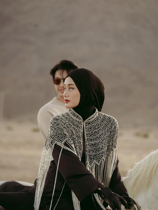Outfit Dinda Hauw sangat cocok dengan suasana gurun pasir yang dramatis, memberikan nuansa Timur Tengah yang kental. Karena itu, banyak netizen menyebutnya mirip warga lokal Madinah. Kepercayaan dirinya saat menunggang kuda juga patut diacungi jempol. (Liputan6.com/IG/@rey_mbayang)
