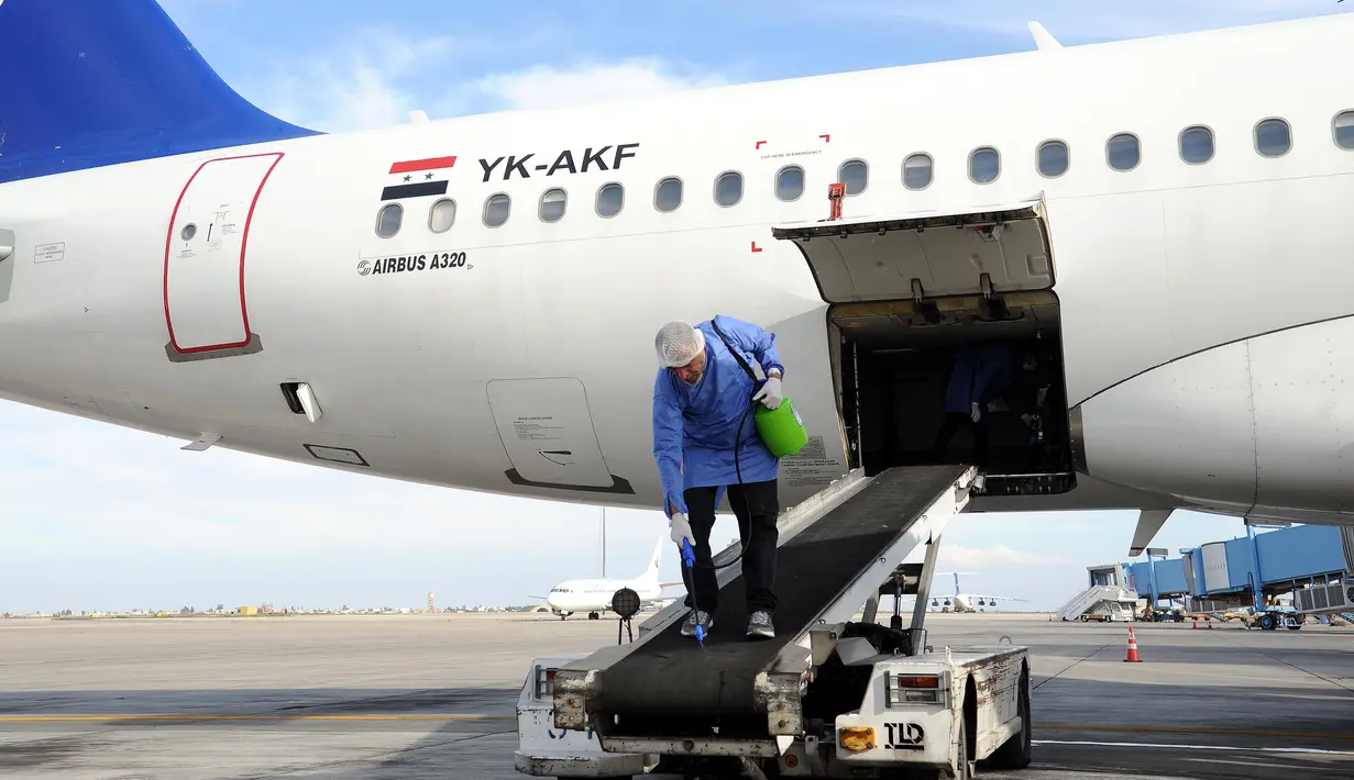 Seorang pekerja menyemprotkan disinfektan sebagai bagian dari langkah untuk memerangi virus corona Covid-19  di luar sebuah pesawat di Bandara Internasional Damaskus, Suriah (16 /3/2020). (Xinhua/Ammar Safarjalani)