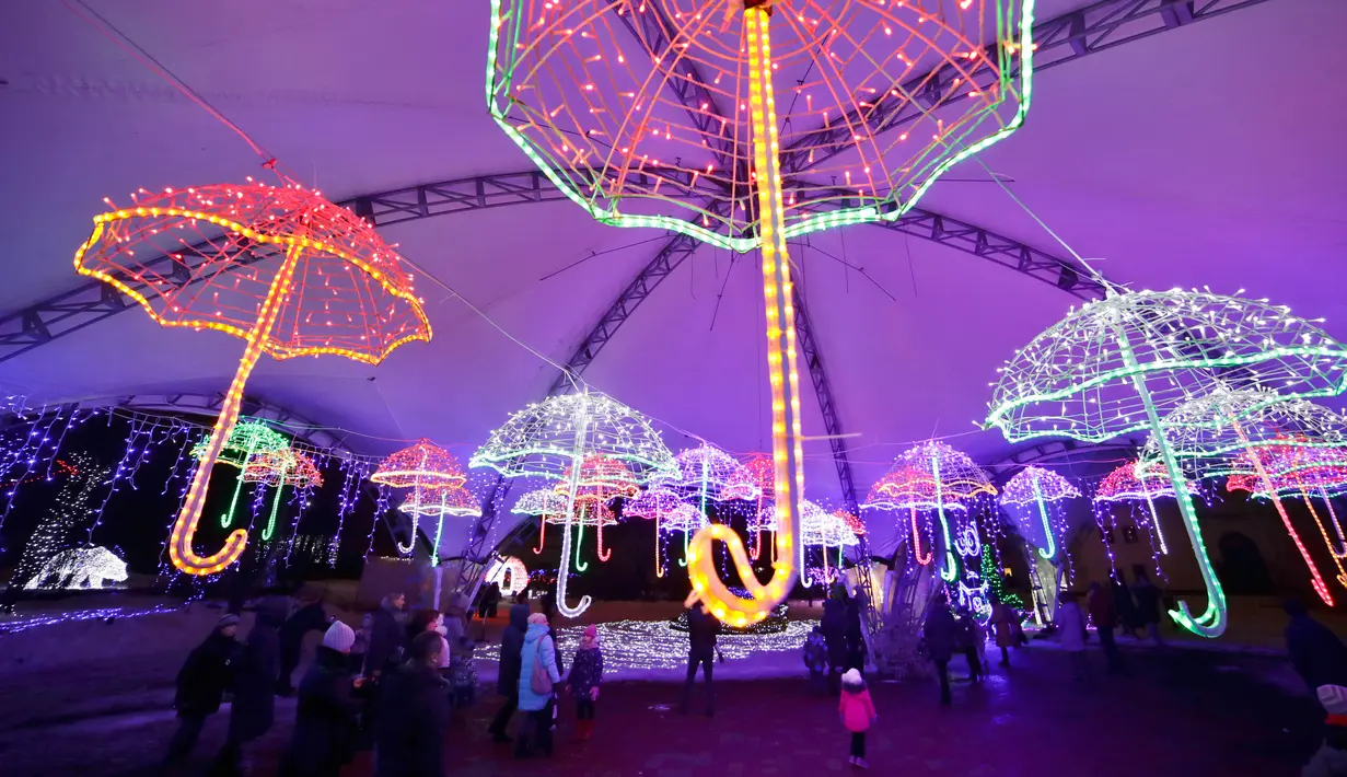 Pengunjung berjalan di dalam hiasan cahaya lampu berbentuk payung di sebuah taman di Minsk, Belarus (28/12). Setelah matahari terbenam, orang-orang berdatangan untuk menikmati pameran cahaya lampu yang dipasang di seluruh taman. (AP Photo/Grits Sergei)