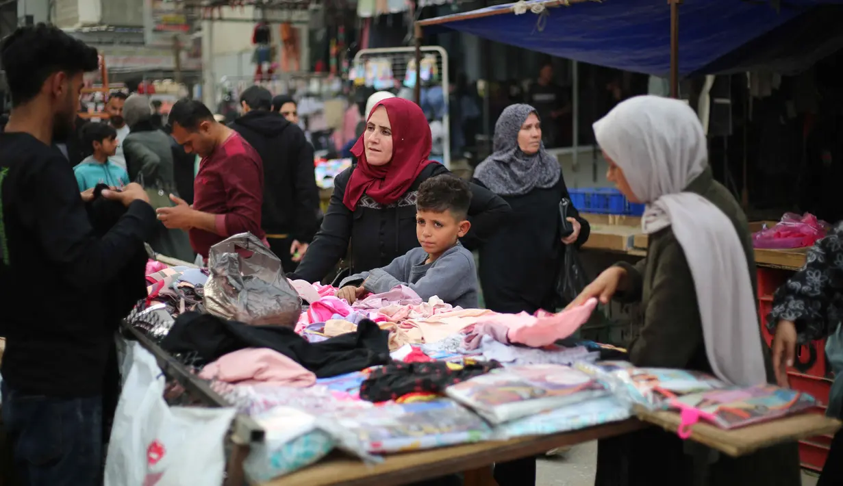 Sebagaimana diketahui, Badan Bantuan dan Pekerjaan PBB untuk pengungsi palestina, UNRWA telah mengumumkan 1,9 juta orang telah mengungsi secara paksa di Jalur Gaza Palestina. Tampak dalam foto, warga Palestina yang mengungsi berbelanja pakaian di pasar jalanan sekitar kamp pengungsi Nuseirat, Jalur Gaza tengah, pada Rabu 18 Maret 2026. (Eyad Baba/AFP)