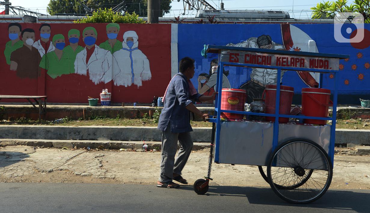 Pedagang lewat depan mural bertemakan COVID-19 di kawasan Manggarai, Bukit Duri, Jakarta, Jumat (28/8/2020). Mural tersebut dibuat untuk meningkatkan kepatuhan masyarakat akan protokol kesehatan karena kasus COVID-19 nasional terus meningkat. (merdeka.com/Imam Buhori)