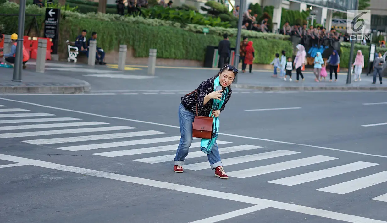 Seorang wanita mengambil foto rekannya dengan latar belakang Jalan MH Thamrin yang masih ditutup oleh aparat keamanan di Jakarta, Jumat (24/5/2019). Ditutupnya Jalan MH Thamrin terkait unjuk rasa menolak hasil Pemilu 2019 dimanfaatkan sebagian warga untuk berfoto. (Liputan6.com/Immanuel Antonius)