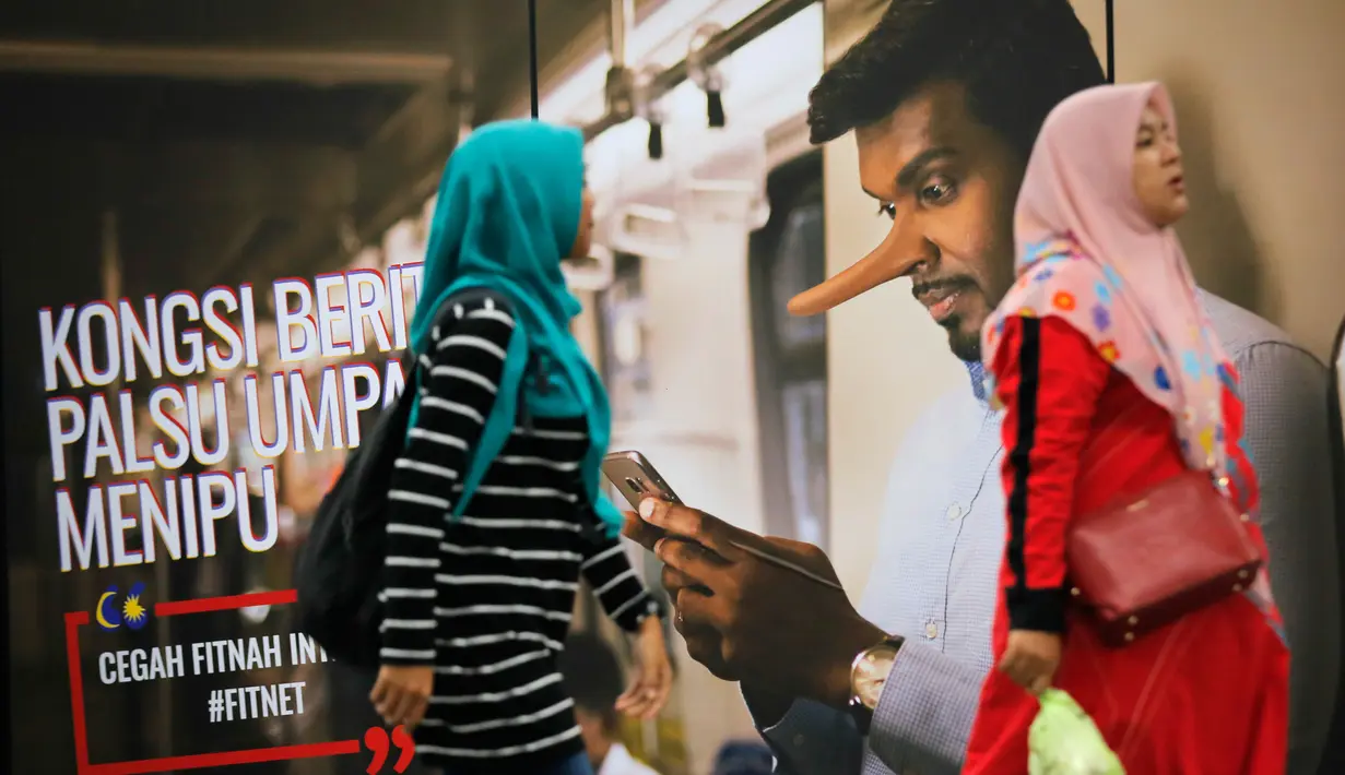Penumpang kereta berjalan dengan latar belakang iklan larangan penyebaran hoax atau berita bohong di Stasiun Kereta Kuala Lumpur, Malaysia, Senin (2/4). Pengesahan UU Antihoax menyebabkan sejumlah pihak khawatir. (AP Photo/Vincent Thian)