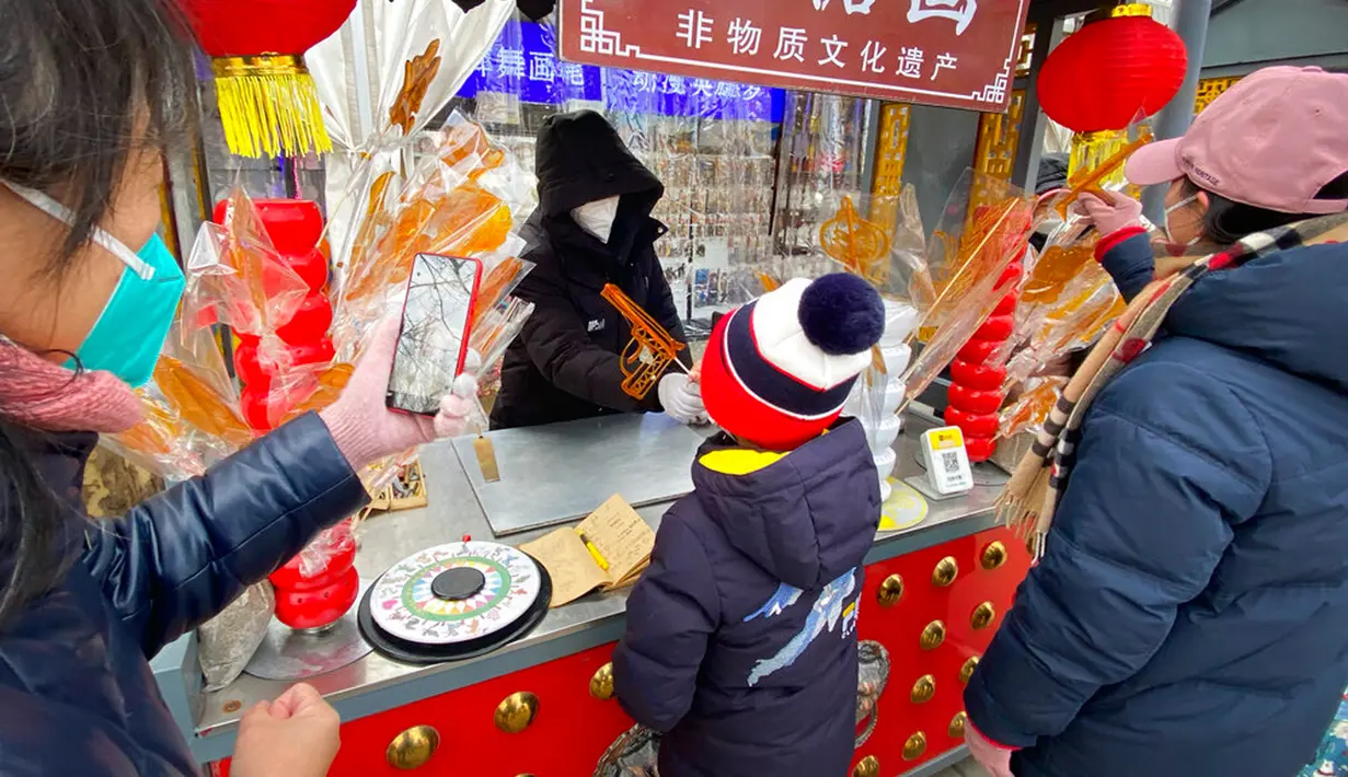 Seorang anak mengambil permen berbentuk pistol dari stan yang disiapkan untuk pekan liburan Tahun Baru Imlek di sebuah taman umum di Beijing, China, Kamis (26/1/2023). (AP Photo/Mark Schiefelbein)