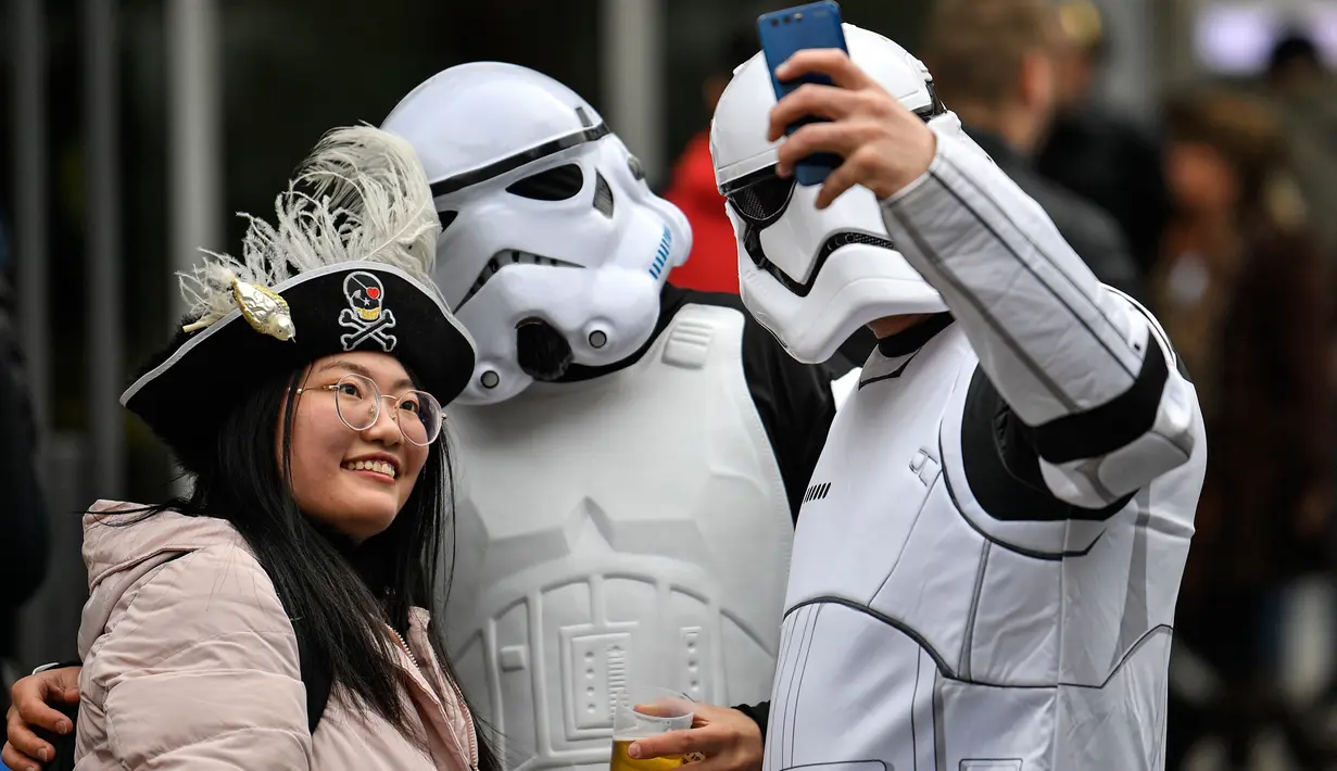 Seorang perempuan berswafoto dengan orang-orang berkostum Stormtrooper, karakter dalam film Star Wars saat puluhan ribu orang bersuka ria merayakan dimulainya musim karnaval di jalan-jalan Kota Cologne, Jerman, Senin (11/11/2019). (AP Photo/Martin Meissner)