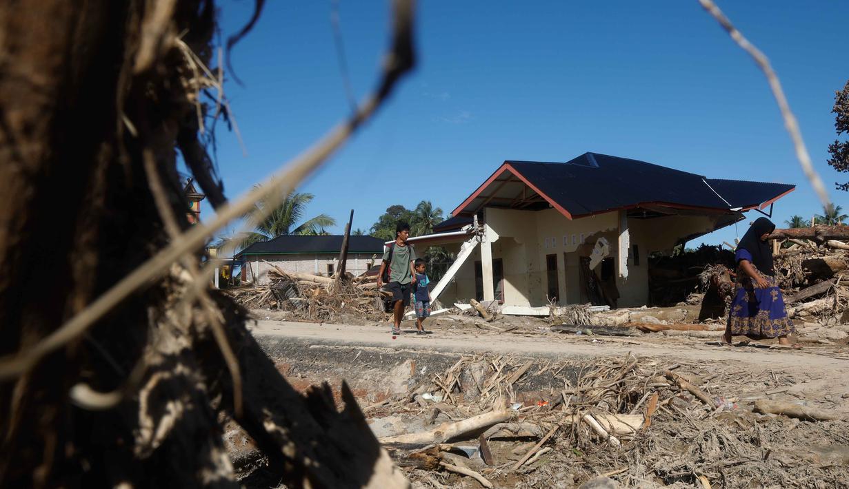 Banyak warga sempat terisolasi karena infrastruktur, termasuk jembatan, hancur diterjang banjir dan material kayu. Tampak dalam foto, warga berjalan melewati reruntuhan rumah di sebuah desa yang terdampak banjir di Batang Toru, Sumatra Utara, Rabu, 3 Desember 2025. (AP Photo/Binsar Bakkara)