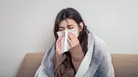Seorang perempuan yang sedang terserang flu menyelimuti tubuhnya di atas sofa dan menutup hidungnya menggunakan tisu (Foto Dok: Freepik/pvproductions).