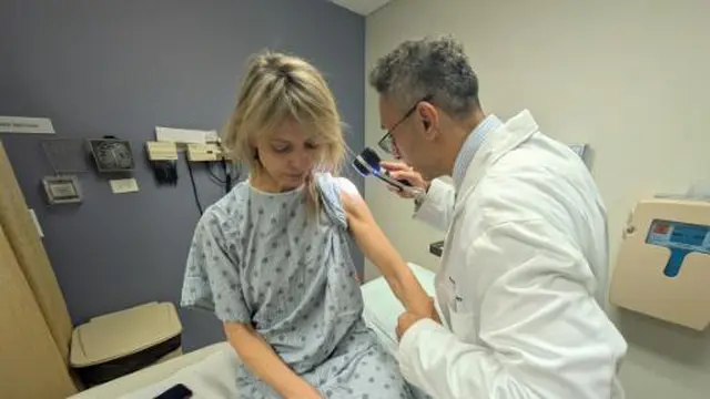 Heidi Tarr, yang didiagnosis menderita melanoma bertahun-tahun setelah rutin menggunakan alat tanning bed, diperiksa oleh dokter kulit Pedram Gerami
