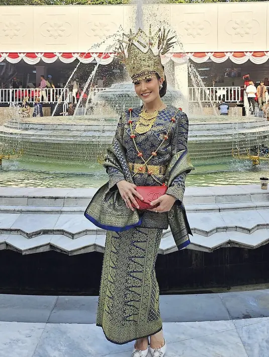 Ayu Dewi hadir mengenakan pakaian khas Lampung terlihat dari mahkota, sabuk, dan kalung yang ia kenakan. Ayu juga tampil dengan kain songket biru keemasan yang dijadikan atasan, rok, dan selendang. [Instagram/mrsayudewi]