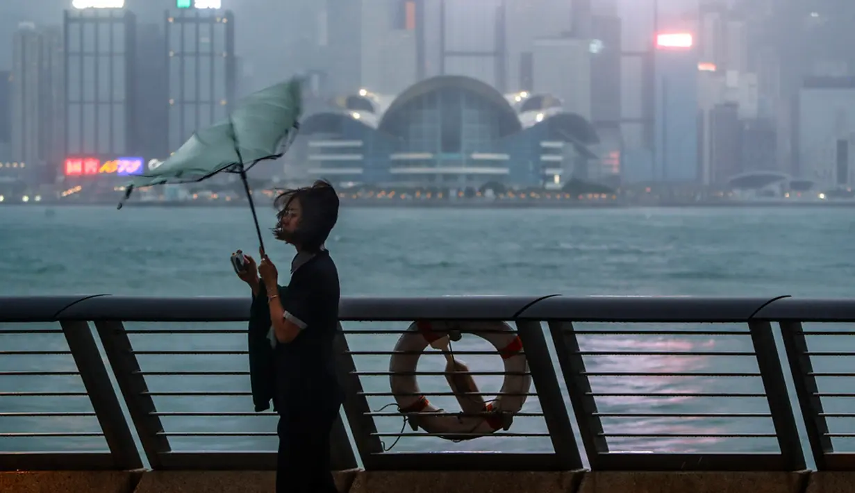 Payung seorang wanita tertiup angin kencang saat Topan Saola melanda Hong Kong, Jumat (1/9/2023). Sebagian besar Hong Kong dan wilayah lain di Tiongkok selatan hampir terhenti dengan aktivitas kelas-kelas dan penerbangan dibatalkan ketika Topan Saola mendekat. (AP Photo/Daniel Ceng)