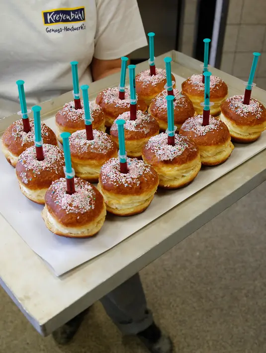 Seorang pekerja memegang nampan berisi berliner (donat Jerman) dengan jarum suntik penuh raspberry jelly di toko roti Kreyenbuhl di Muri, Swiss, 5 Februari 2021. Pembeli dapat menyuntikkan sendiri "vaksin" ke dalam donut dengan pilihan rasa raspberry atau Bailey-liqueur. (STEFAN WERMUTH/AFP)