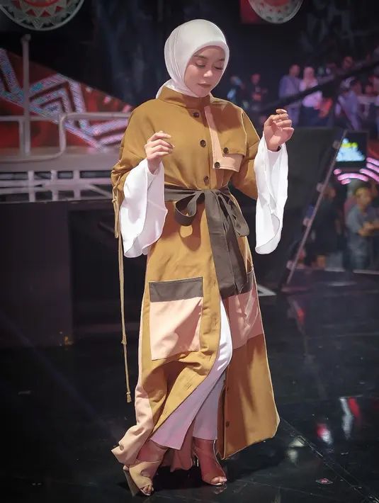 Berpose di panggung sebuah acara, Lesti Kejora mengenakan luaran warna soga lengan pendek yang memanjang menutupi kaki. Luaran ini membalut busana muslim putih polos berlengan mengembang yang dipadukan dengan jilbab warna senada. Bergaya setengah menunduk seolah menghindari kamera, pose ini panen pujian. Lebih dari 170 ribu orang mengirim tanda hati. (Foto: Dok. Instagram @lestykejora)