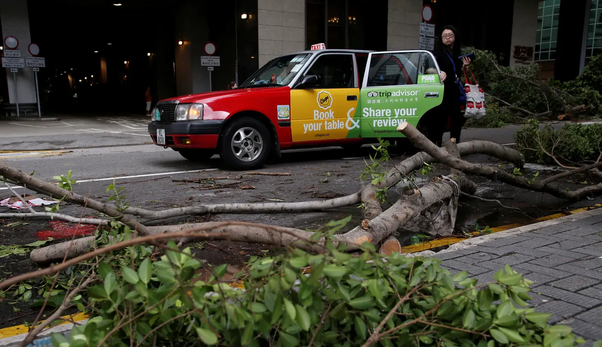 Warga turun dari taxi dekat dengan pohon yang tumbang akibat angin yang kuat di Hong Kong, China, 2 Agustus 2016. Angin kencang berkekuatan 151 kilometer per jam itu membuat bandara, sekolah dan perkantoran tutup. (REUTERS/Tyrone Siu)