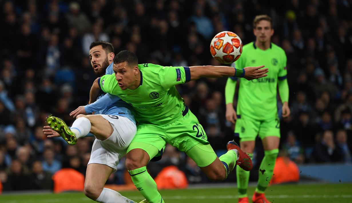 Bernardo Silva menjatuhkan Jeffrey Br pada leg kedua, babak 16 besar Liga Champions yang berlangsung di Stadion Etihad, Manchester, Rabu (13/3). Man City menang 7-0 atas Schalke. (AFP/Paul Ellis)