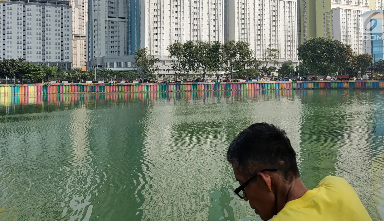 Seorang warga mengamati Danau Sunter yang berwarna hijau di Jakarta Utara pada Senin (8/7/2019). Lamanya musim kemarau di Ibu kota menjadi penyebab danau tersebut berubah warna menjadi hijau yang dipicu oleh pertumbuhan lumut. (Liputan6.com/Immanuel Antonius)