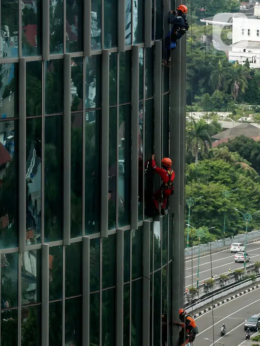 Pekerja saat membersihkan kaca gedung bertingkat di kawasan Kuningan, Jakarta, Minggu (19/12/2021). Pekerja ini harus bergelantungan dengan seutas tali untuk membersihkan dinding-dinding gedung bertingkat yang tingginya kurang lebih mencapai 150 meter. (Liputan6.com/Johan Tallo)